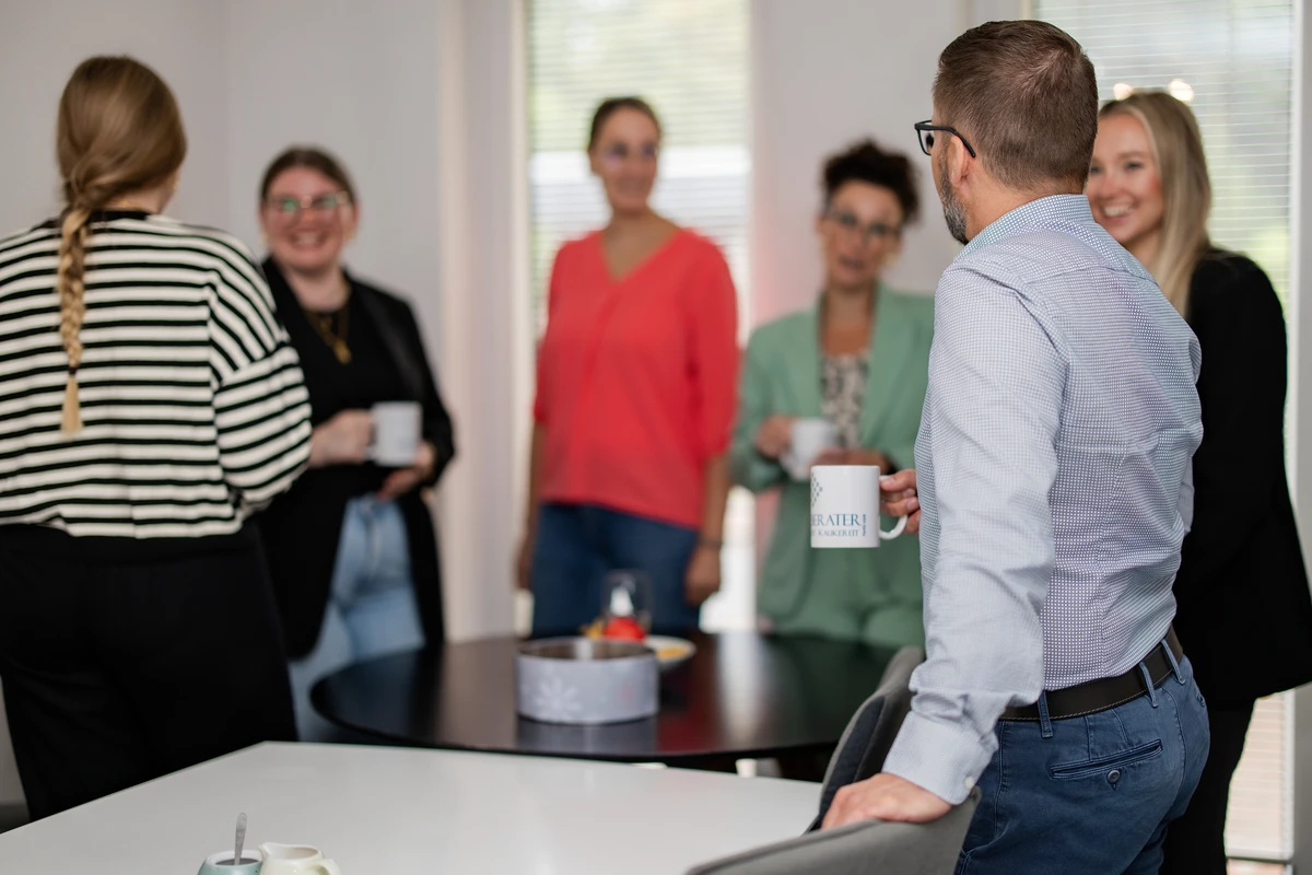 Angenehme Arbeitsatmosphäre bei Steuerberater RKK – Ein Team, das zusammenhält Team von Steuerberater RKK steht zusammen bei einer fröhlichen Kaffeepause mit Kerze auf dem Tisch
